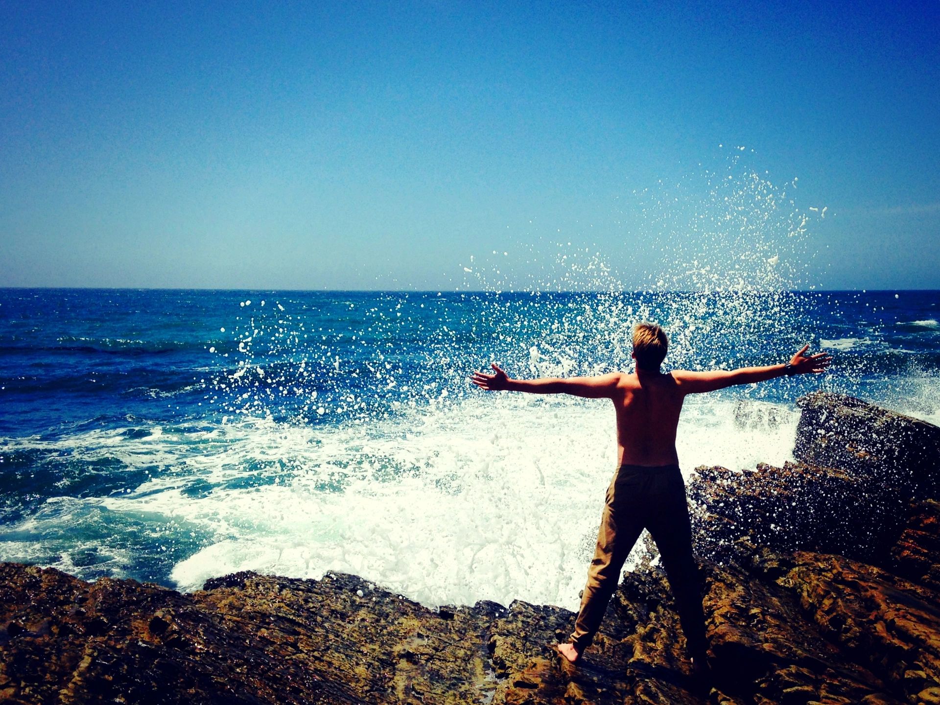 Man standing on rocks at the beach with open arms taking in the waves and demonstrating freedom