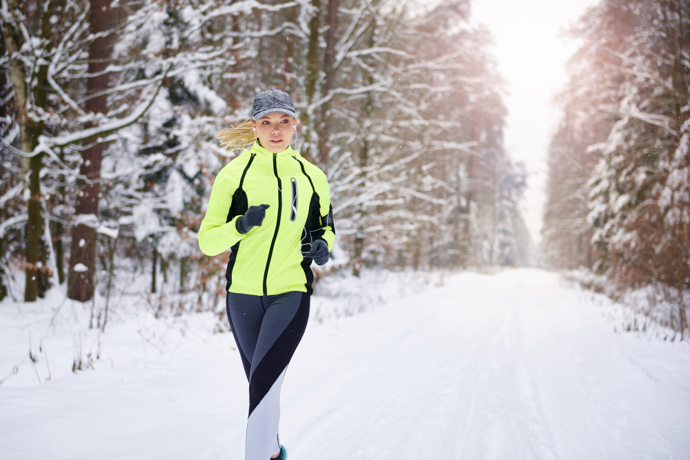 Woman running in a forest during winter with reflective jacket and earphones
